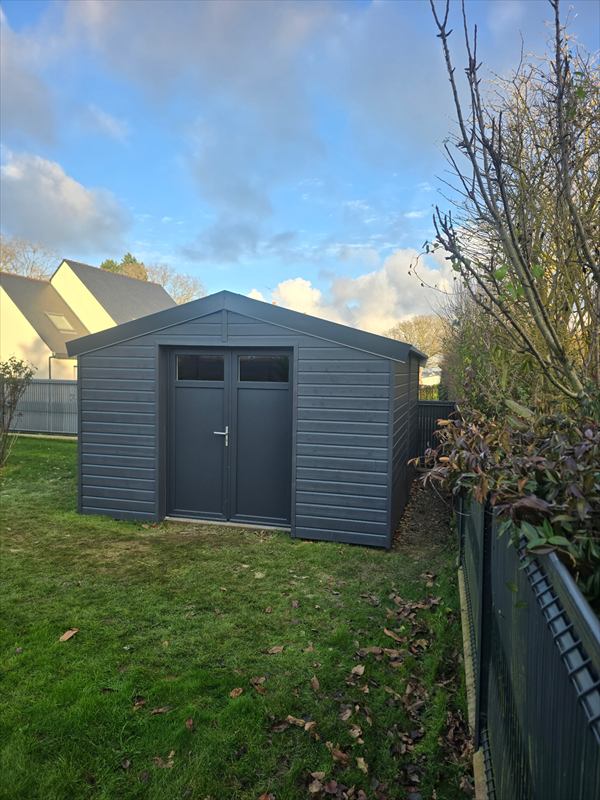 Abri de jardin en bois bardé anthracite, double porte vitrée, posé sur une pelouse