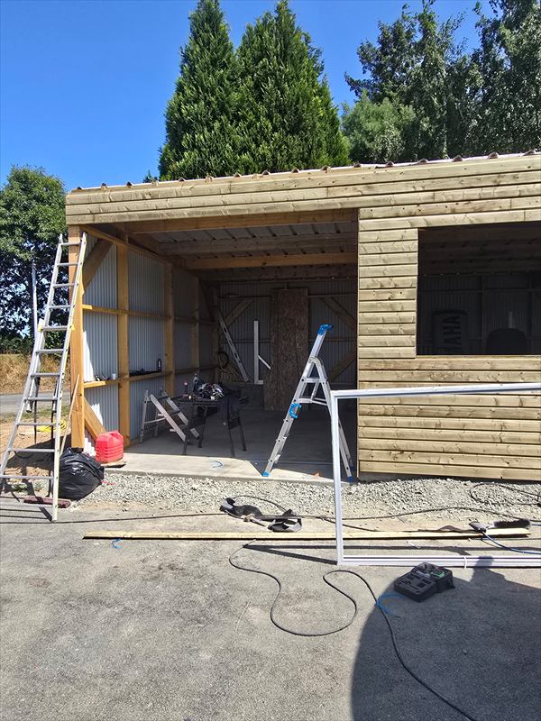 Bâtiment en ossature et bardage bois avec un auvent ouvert sur poteaux, bardage acier à l'intérieur, chantier en cours