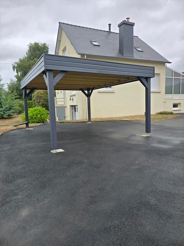 Carport adossé au pignon d'une maison, poteaux et bandeau anthracite, sous-face en bois