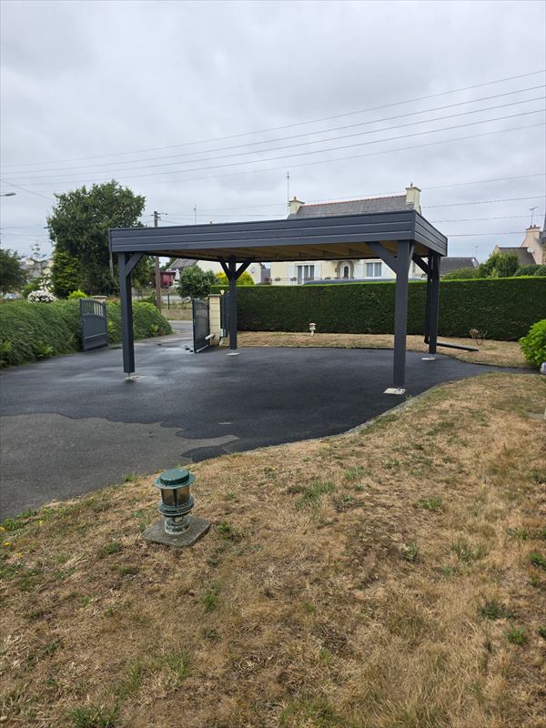 Le même carport autoportant vu depuis la pelouse, poteaux anthracite fixés sur platines